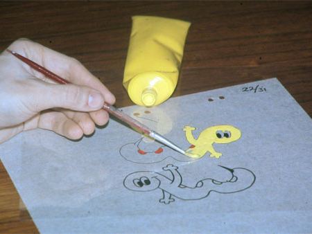 A hand painting colour onto the back of a transparent animation cel