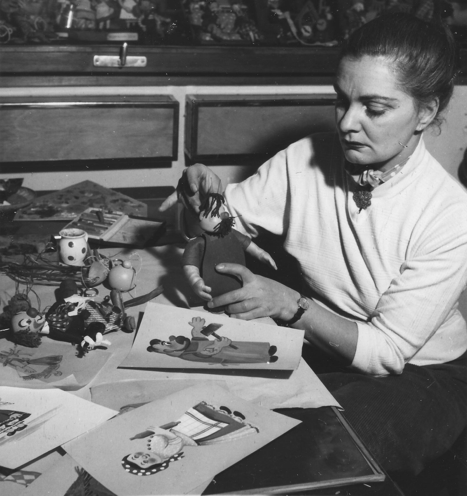 Filmmaker Éva Balla-Falus posing small puppets on a table in a puppet animation studio in 1955